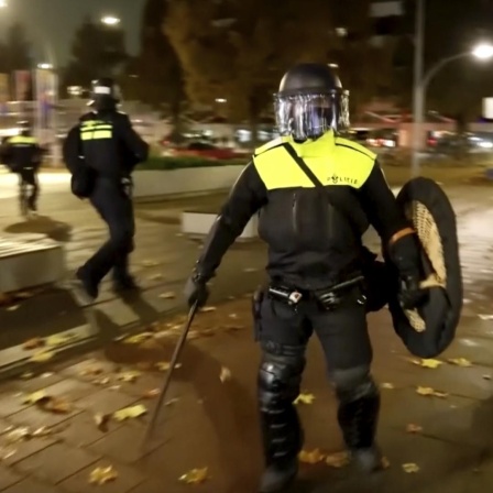 In Amsterdam gab es erneut Krawalle. Polizisten laufen am Abend durch eine Straße. 