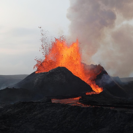 Ein Vulkanausbruch, die Lavawolke steigt auf und läuft am Berg herunter.