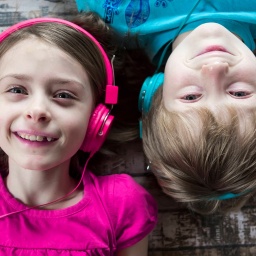 Porträt von einem Mädchen und einem Jungen, die mit Kopfhörern auf dem Rücken liegen.