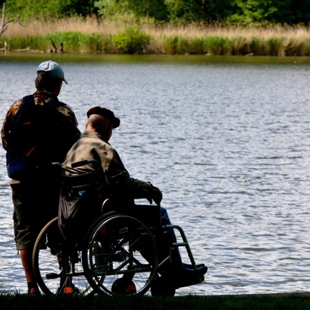 Ein Mann begleitet einen älteren Herren in einem Rollstuhl