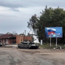Ein zurück gelassener russischer Panzer auf einer zerstörten Straße in Izjum, Ukraine. Im Hintergrund ist ein Plakat mit der Flagge Russlands zu sehen.