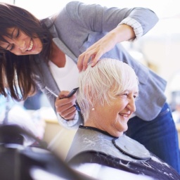 Friseurin schneidet Kundin die Haare, beide lächeln. 