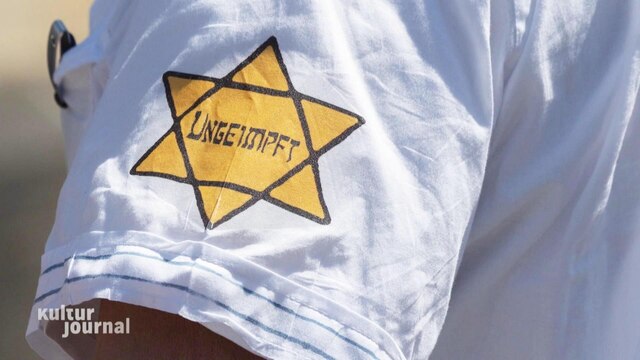 Nahaufnahme von einem weißen T-Shirt-Ärmel. Darauf befindet sich ein gelber Davidstern im Stil des Judensterns im Dritten Reich. Darin steht: "Ungeimpft".