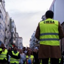 Redner mit gelber Warnweste, auf der die Worte "Chega" stehen, spricht zu einer Gruppen von Menschen, die ebenfalls Warnwesten tragen, vor ihm