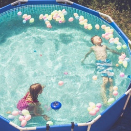 Ein Mädchen und ein Junge in einem Pool mit ganz vielen Luftballons.