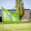 Vor einem Stall weht die grüne Fahne der BoerBurgerBeweging. Darauf sind drei Bs und ein Kleeblatt.