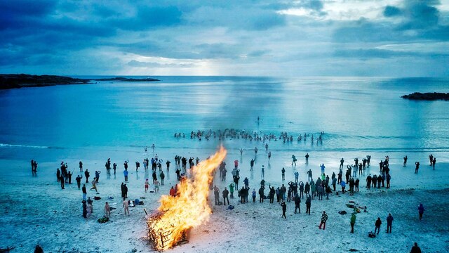 Viele Menschen laufen ins Meer. Am Strand lodert ein großes Lagerfeuer.