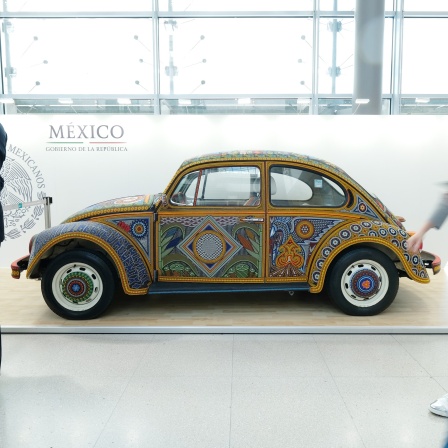 Ein VW-Käfer mit Bemalung in einem mexikanischen Ornament-Stil steht vor einer Wand mit der Aufschrift &#034;México&#034; in einer Ausstellungshalle.