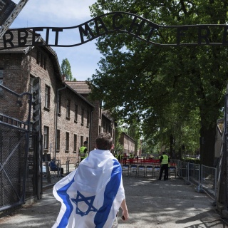 Jüdischer Jugendlicher mit der Israel-Flagge vor dem Eingang zum Nazi-Konzentrationslager Auschwitz mit dem Schriftzug &#034;Arbeit macht frei&#034;