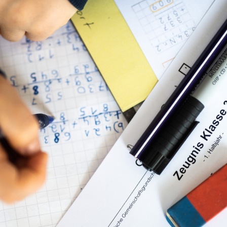 Eine Schülerin der dritten Klasse arbeitet an ihrem Schreibtisch, während ihr Zeugnis auf ihrem Schreibtisch liegt.