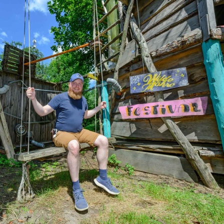 Alexander Dettke, Gründer vom "Wilde Möhre" Festival, sitzt auf einer Schaukel neben einem Baumhaus auf dem Festivalgelände (Bild: picture alliance/dpa/Patrick Pleul)