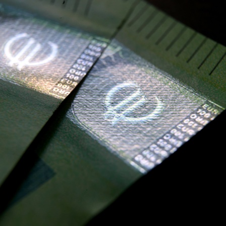 Zwei 100-Euro-Banknoten liegen auf einem Tisch - die Euro-Symbole leuchten im sonst diffusen Licht auf.