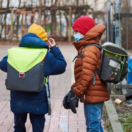Zwei Schüler, die medizinische Masken tragen, kommen mit Schulranzen zum Eingang einer Grundschule in Prenzlauer Berg.
