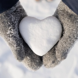Ein Herz aus Schnee liegt in zwei Händen mit Handschuhen.