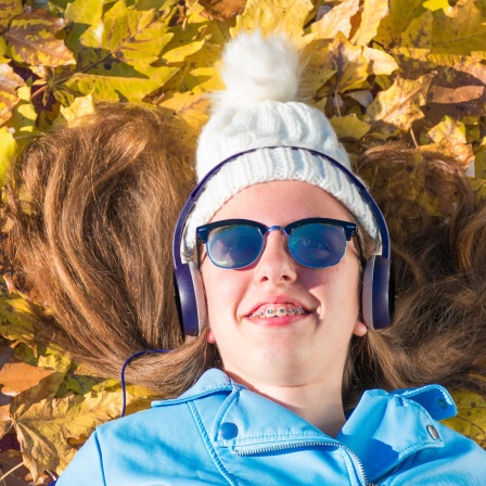 Mädchen liegt im Herbstlaub und hört mit Kopfhörern