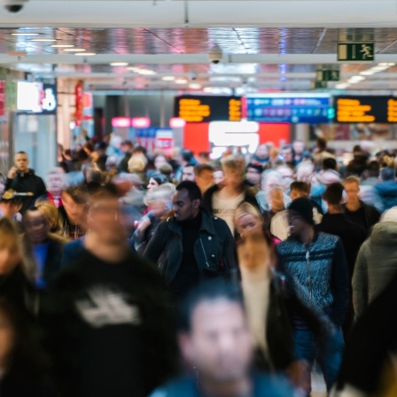 Im Hauptbahnhof Hannover sind zahlreiche Menschen zu sehen, im Hintergrund Anzeigetafeln.