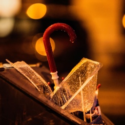 Ein kapuuter nasser Regenschirm steckt nach einem Karnevalszumzug in einem Mülleimer. Durch das Licht der Laternen glitzert die Oberfläche. 