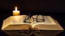 Aufgeschlagene Bibel mit Kerze. Brille auf der Bibel.
