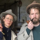Ein Mann und eine Frau posieren in Trenchcoat und Hut mit Zigarette und Pfeife als Kommissare.