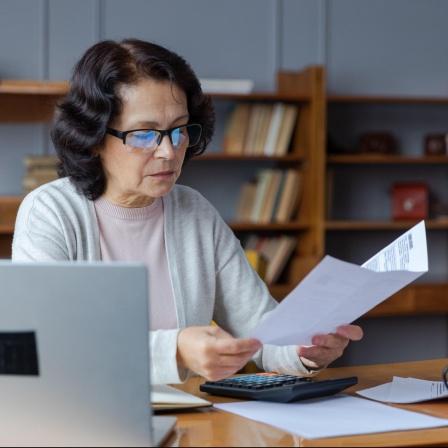 Ein Frau sitzt an einem Arbeitschtisch und schaut auf einen Zettel.