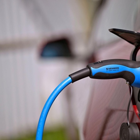 Öffentliche Ladesäule für E-Autos an einem Parkplatz.  Ein Tesla Model 3 lädt gerade seinen Akku an der Stromtankstelle voll, der Stecker steckt im Ladeanschluss des Autos.