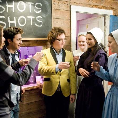 Symbolbild: Filmstill aus der amerikanischen Komödie Spritztour (original: "Sex Drive) zeigt in einer Szene eine Rumspringa Party. Traditionell gekleidete, weibliche Amish stehen neben anderen Jugendlichen und stossen gegenseitig mit "Shots" an.