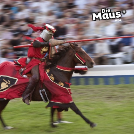 Auf dem Bild ist ein Ritter in roter Rüstung auf einem galoppierenden Pferd während eines Lanzenturniers zu sehen, mit verschwommenen Zuschauern im Hintergrund und dem "Die Maus"-Logo in der oberen rechten Ecke.