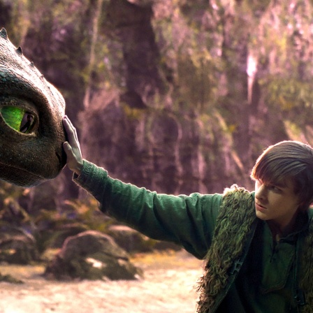 Eine junge Person hält einen schwarzen Drachen mit grünen Augen vorsichtig an der Schnauzen - Szene aus dem Kinofilm "Drachenzähmen leicht gemacht"