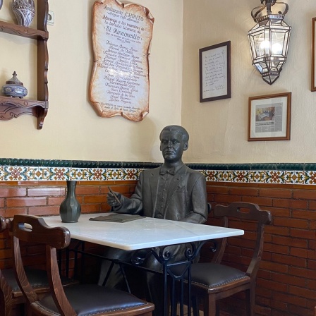 Eine Bronzefigur sitzt in einem traditionallem Restaurant in Granada - die Figur stellt den Dichter Federico García Lorca dar