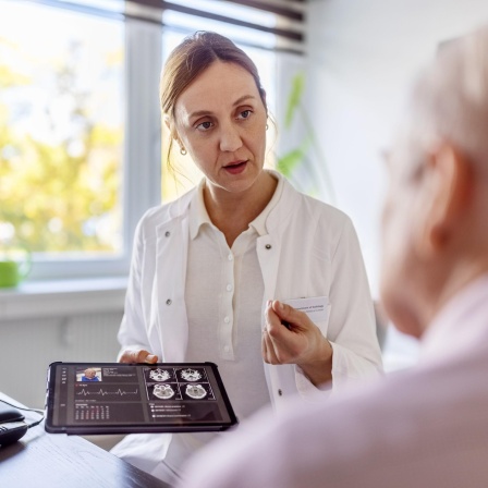 Eine Ärztin hält ein Tablet mit einem Röntgenbild und erklärt einem Patienten etwas daran.