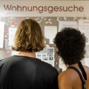 Ein Paar steht vor einer Anzeigentafel mit der Aufschrift "Wohnungsgesuche" an der Uni in Bonn.