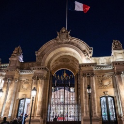 Über dem erleuchteten Elysee-Palast in Paris weht in der Dunkelheit eine Frankreich-Fahne.