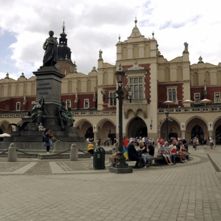 Blick über einen Platz mit einer Statue auf großes Gebäude mit Laubengang