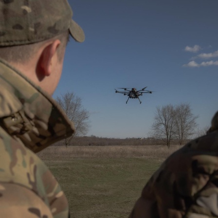 Zwei Militärangehörige beobachten eine Drohne, die über einem Feld aufsteigt.