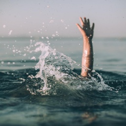 Eine winkende Hand ragt aus einer aufgewühlten Wasseroberfläche hervor.