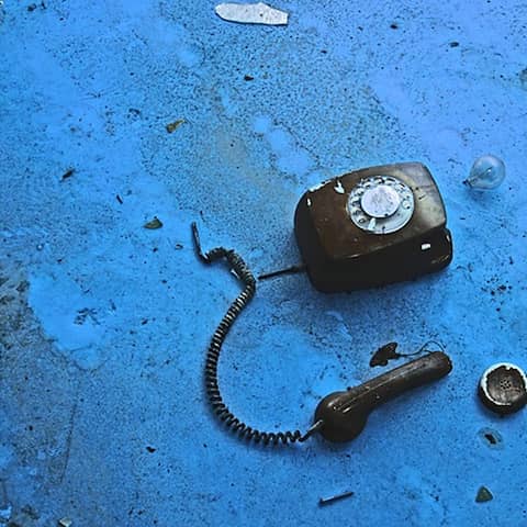 Ein ramponiertes schwarzes Telefon auf blauem Grund (Foto: Stefan Kuhnigk l photocase.com)
