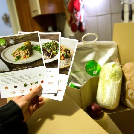 Ein Mann hält mitgelieferte Kochrezepte aus einer HelloFresh Kochbox in der Hand.