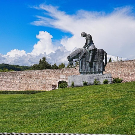 Franziskusstatue von Norberto Proietti: Franziskus reitet in voller Rüstung, den Oberkörper vornüber gebeugt. Er kehrt krank und demütig aus dem Krieg nach Assisi zurück.