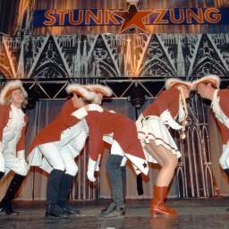 Menschen stehen in Karnevalsuniform auf einer Bühne, Logo und Schriftzug "Stunksitzung".