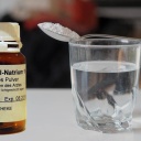 Ein braunes Arzneimittelglas mit Pentobarbital-Natrium, daneben ein gefülltes Wasserglas, auf dem ein Löffel mit dem Pulver liegt. Das tödlich wirkende Mittel wird in der Schweiz beim assistierten Suizid verwendet