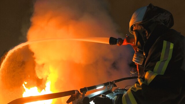 Ein Feuerwehrmann in Schutzkleidung auf einer Drehleiter löscht einen Brand.