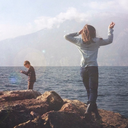 Ein Mädchen und ein Junge spielen auf Steinen vor einem See.