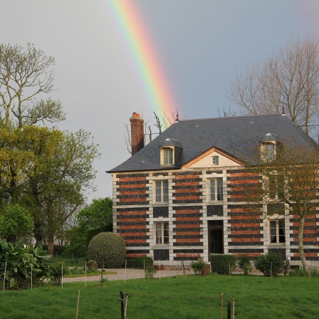 Über einem von Bäumen umgebenen Landhaus steht ein Regenbogen