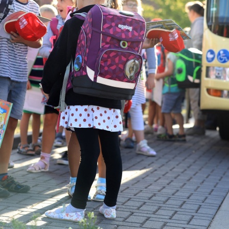 Kinder stehen mit ihrem Ranzen vor einem Schulbus.