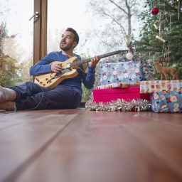 Ein Mann sitzt vor einem Weihnachtsbaum und musiziert mit einer E-Gitarre