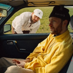 Ein Mann sitzt mit gelbem Fleecepulli und Mütze auf dem Beifahrersitz. Ein anderer Mann ist durch das geöffnete Fenster der Beifahrertür zu sehen. Er trägt einen weißen Pulli.  | Bild: Ferge x Fishermann Instagram