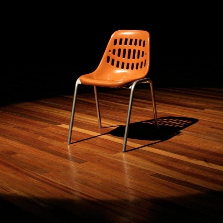 Ein leerer Stuhl steht auf einer Theaterbühne.
