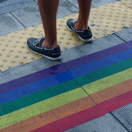 Symbolbild: Ein Mensch steht auf einem Fußweg mit regenbogenfarbener Bemalung