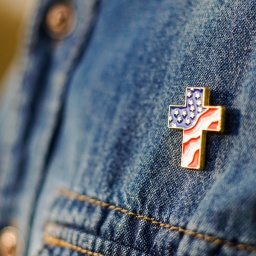 Eine Person mit Jeansjacke trägt einen Anstecker in Form eines Kreuzes, der mit den Stars and Stripes der amerikanischen Flagge gefüllt ist