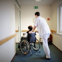Ein Pfleger schiebt eine Frau im Rollstuhl durch einen Gang